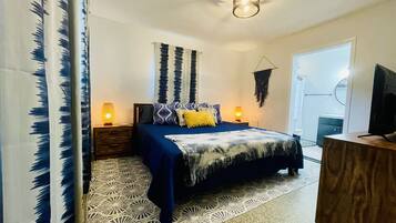 Une chambre à coucher avec un lit, deux tables de chevet avec des lampes, une tapisserie murale et un téléviseur posé sur un meuble en bois.