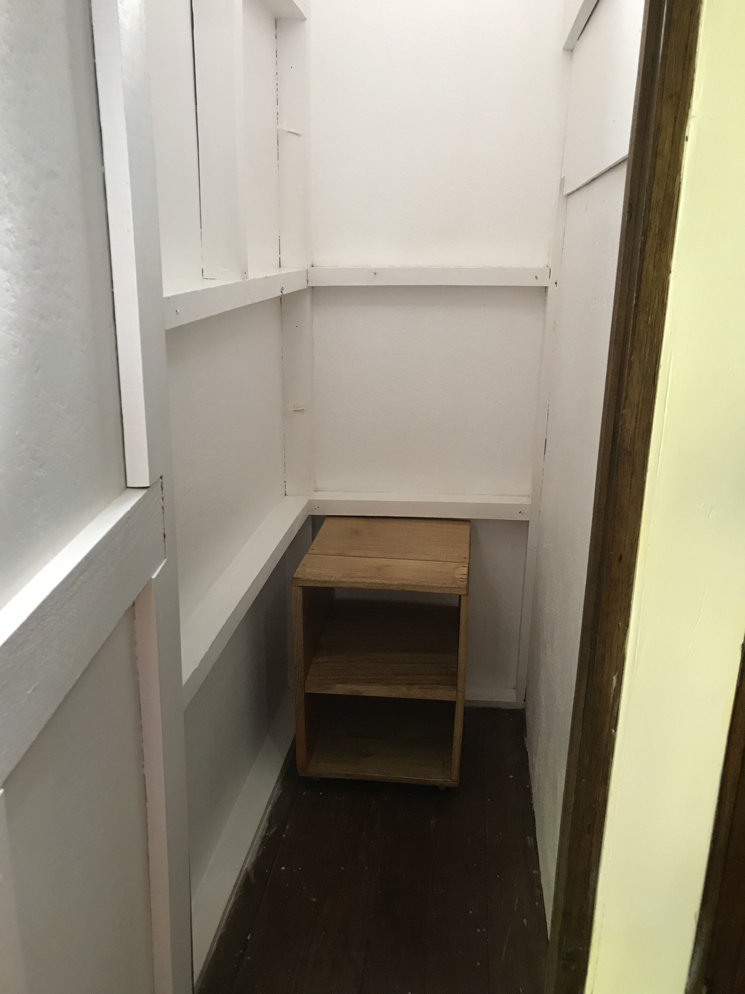 A narrow hallway with white walls and a wooden shelf unit.