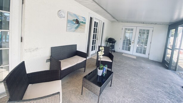 A covered patio area with wicker furniture, a painting, and a grill.
