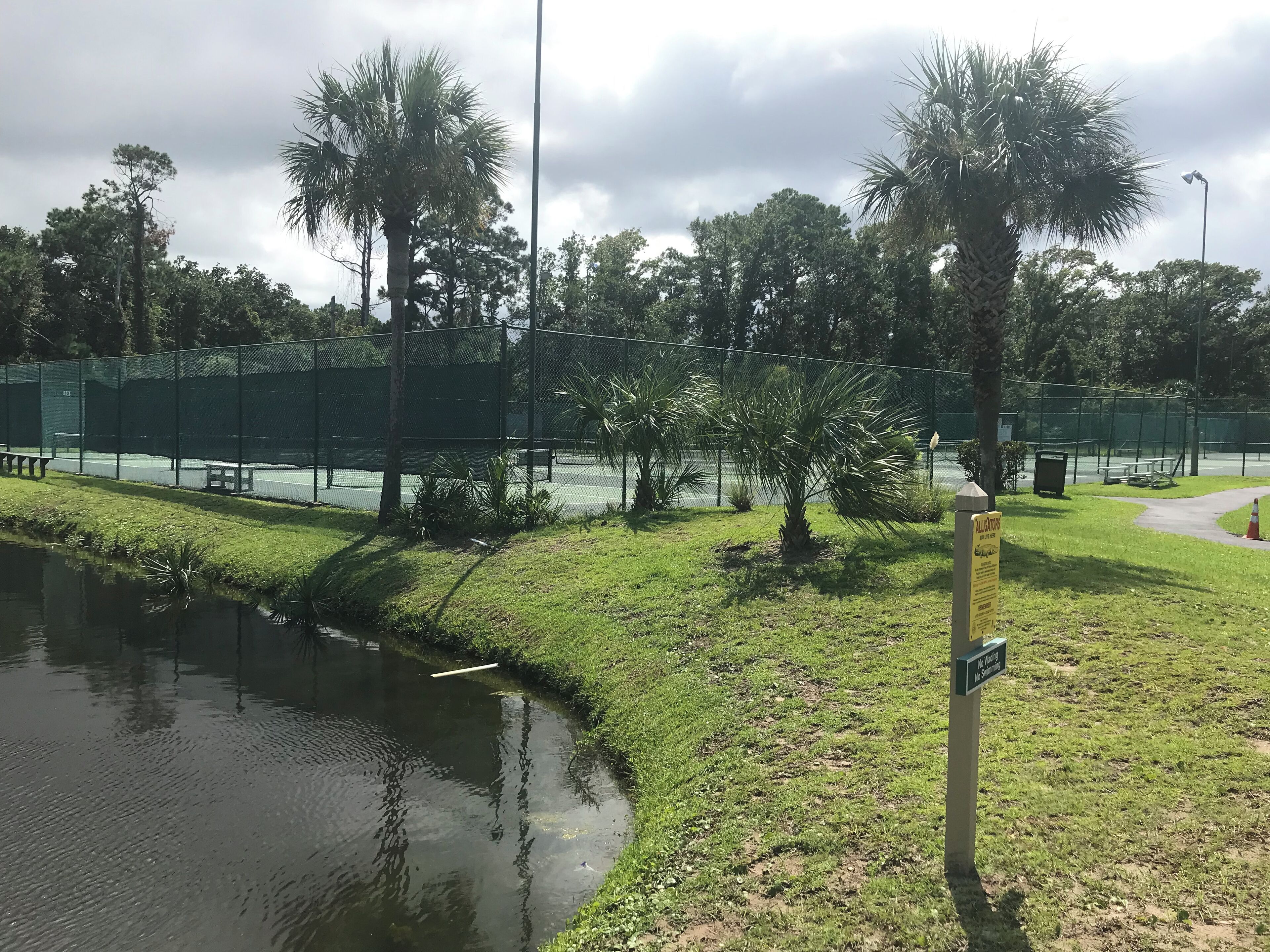 Una cancha de tenis cercada con una fuente de agua y palmeras.