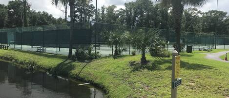 Una cancha de tenis cercada con una fuente de agua y palmeras.