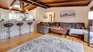 Un interior moderno con techo de madera, una zona de cocina, un sofá seccional gris y una alfombra estampada.