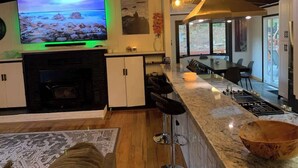Una cocina moderna con un televisor grande, taburetes de bar, chimenea y comedor con una mesa grande y sillas.