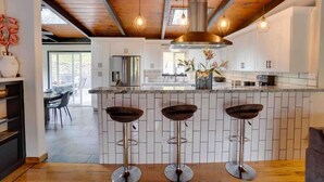 Una cocina moderna con baldosas blancas tipo metro, una isla central con taburetes y vigas de madera a la vista.