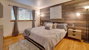 Un dormitorio con cama, mesita de noche, lámpara, ventana con cortinas y un panel de madera en la pared.