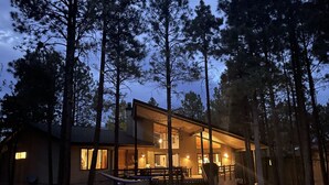 Eine moderne Holzhütte mit großer Terrasse und zahlreichen Fenstern, umgeben von hohen Kiefern.