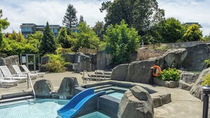 Un área de piscina con un tobogán azul, sillas de descanso y un puesto de salvavidas.