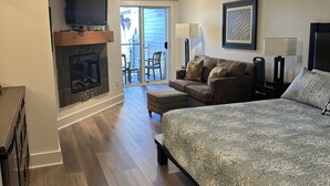 Un dormitorio con una cama grande, un televisor montado en un estante de madera, una chimenea y un balcón con mobiliario exterior.