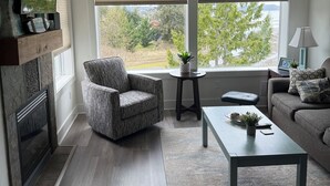 Una sala de estar moderna con chimenea, ventilador de techo, sofá, mesa de centro y vistas a un lago.