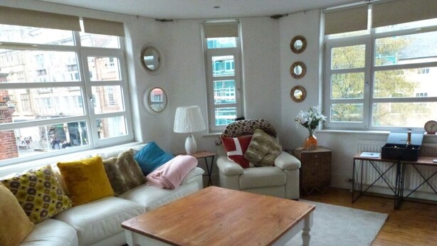 Un salón con un sofá blanco, una mesa de centro de madera y una ventana con vistas a edificios.