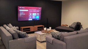 A modern living room with a flat-screen TV mounted on the wall, grey sofas, a wooden coffee table, and a patterned rug. - WALK TO PRIVATE ACCESS  "PET FRIENDLY BEACH"  ENJOY 
PRIVATE POOL & HOT TUB (Gulf Shores)