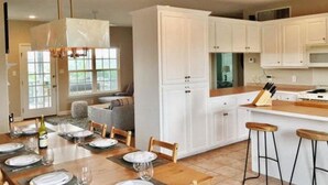A modern kitchen with white cabinets, a dining table set for four, and a bar area with stools. - WALK TO PRIVATE ACCESS  "PET FRIENDLY BEACH"  ENJOY 
PRIVATE POOL & HOT TUB (Gulf Shores)