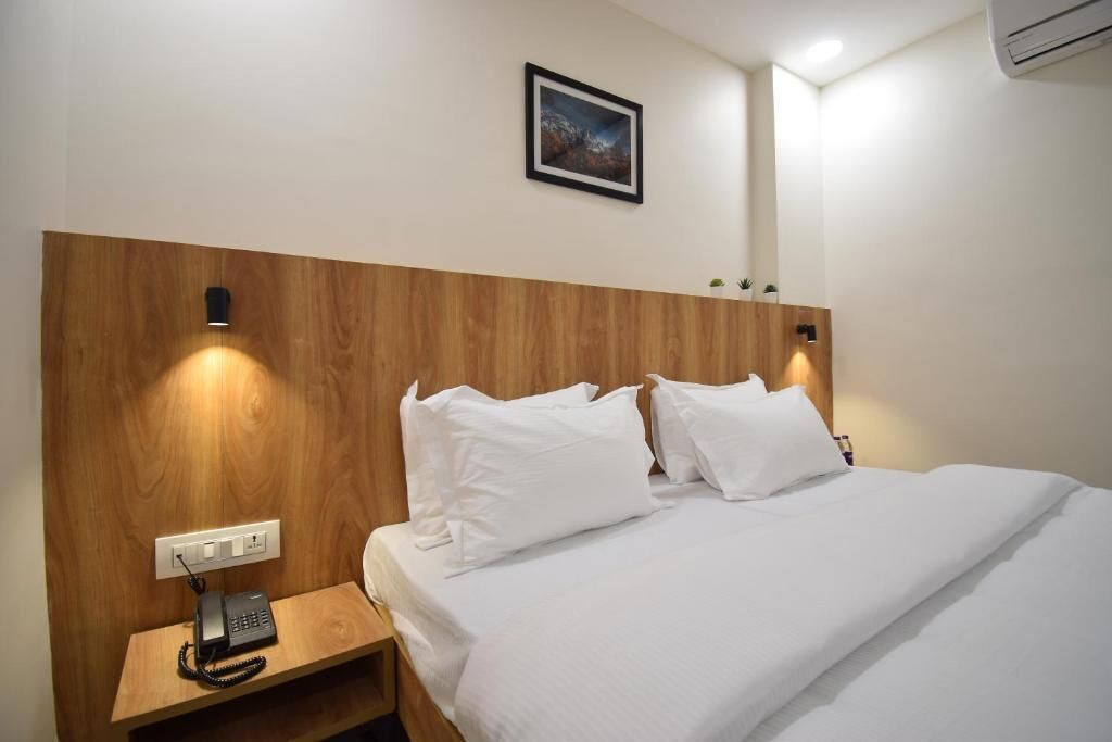 Habitación de hotel con cabecera de madera, cama con sábanas blancas, teléfono en la mesita de noche y un cuadro en la pared.