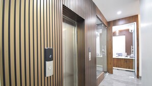 Un ascensor moderno con paneles de madera, un área de recepción con mostrador y una partición de vidrio, y un suelo limpio de baldosas.