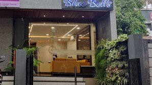 Entrada moderna del hotel Blue Bells, con fachada de vidrio, zona de estar interior y plantas en macetas.