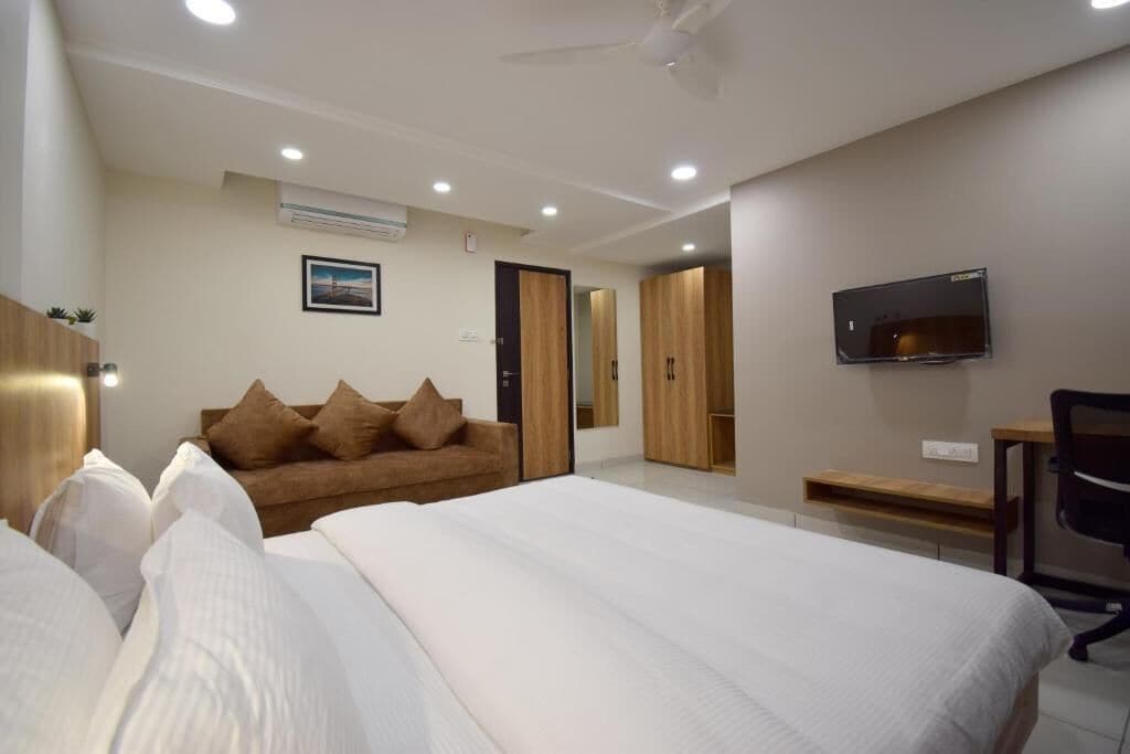 A hotel room with a large bed, a sofa, a desk, and a TV.