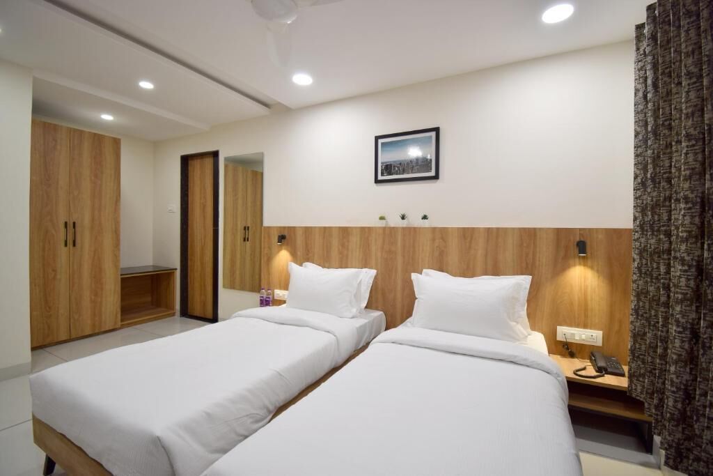 Hotellihuone, jossa on kaksi erillistä sänkyä, puinen vaatekaappi, pieni pöytä, jossa on puhelin, ja taulu seinällä.