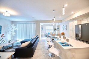 Enjoy a spacious living area with a sofa, dining area with a bar, and a kitchen equipped with a large refrigerator and sleek countertop.