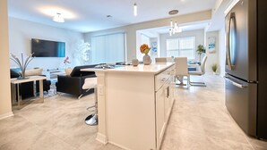 Una cocina moderna con una isla central, un comedor con mesa y sillas, y una sala de estar con sofá y televisión.