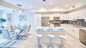 Una cocina moderna con armarios blancos, electrodomésticos de acero inoxidable y una isla central con taburetes de bar.