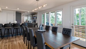 Een moderne keuken met een centraal eiland, barkrukken en een eethoek met een grote tafel en stoelen.