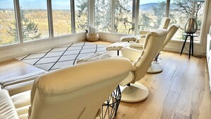 Een kamer met grote ramen, een geometrisch vloerkleed en meerdere fauteuils.