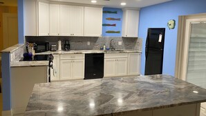 A kitchen with white cabinets, a marble countertop, a black refrigerator, and a coffee maker.