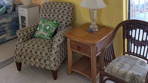 A living room with a patterned armchair, a wooden side table with a lamp, and a decorative wall piece.