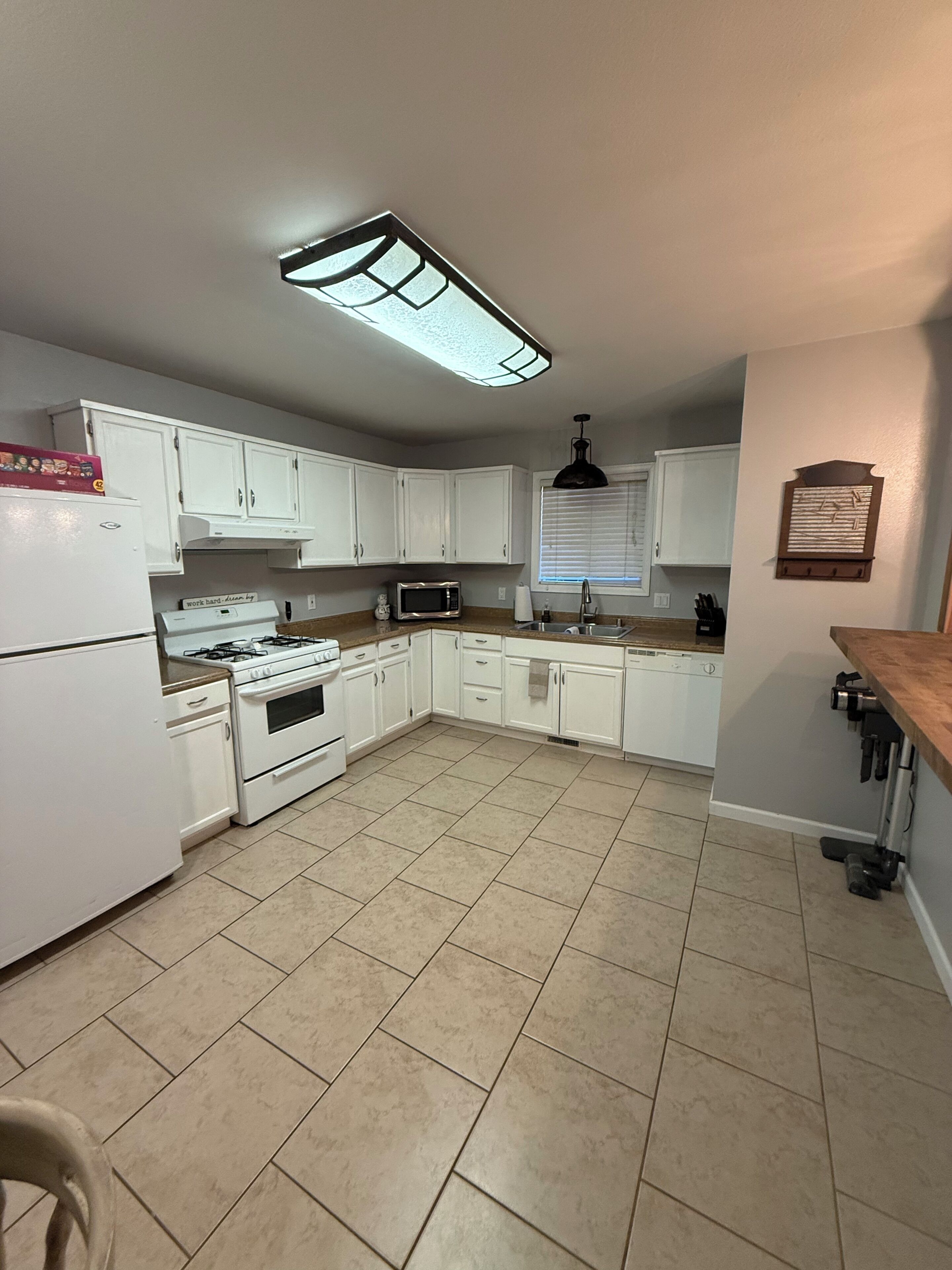 A kitchen with white cabinets, a stove, a microwave, and a window with blinds.