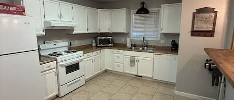 A kitchen with white cabinets, a stove, a microwave, and a window with blinds.