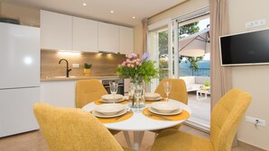Een moderne keuken met witte kasten, een eettafel met gele stoelen en uitzicht op het groen door een schuifdeur.