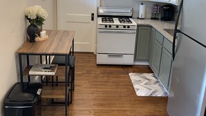 Une cuisine compacte avec des meubles blancs, un four à micro-ondes, une cuisinière et un réfrigérateur. On y trouve une table à manger en bois, ornée d’un vase de fleurs et d’un livre.