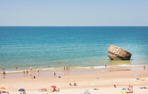 A beach with clear blue water, a large rock formation, and people sunbathing and swimming. - 3 bedroom awesome home in Matalascañas (Matalascañas)