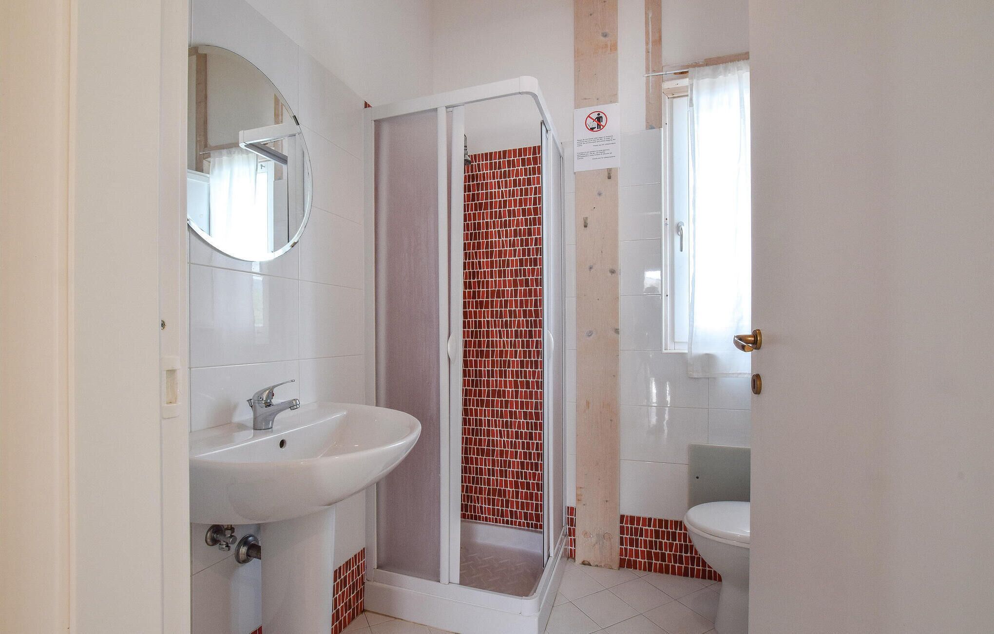 Une salle de bain avec un lavabo blanc, un miroir, une douche aux carreaux de mosaïque rouge et des toilettes.