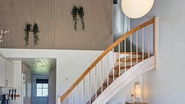 Ein modernes Interieur mit einer Holztreppe, einer gestreiften Wand und einer hängenden Pflanze.