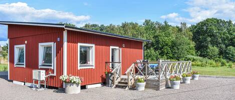 A red building with a gravel driveway and a wooden deck with chairs and potted plants.