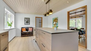 Une cuisine moderne dotée d’un îlot central, d’un plafond en bois et d’un coin repas baigné de lumière naturelle.