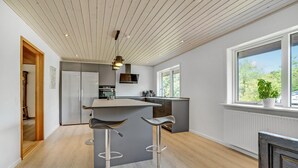 Une cuisine moderne dotée d’un îlot central, de tabourets de bar et d’une grande fenêtre offrant une vue sur la verdure.