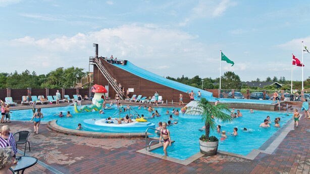 Un espace piscine comprenant un toboggan, des chaises longues et un élément décoratif aquatique.