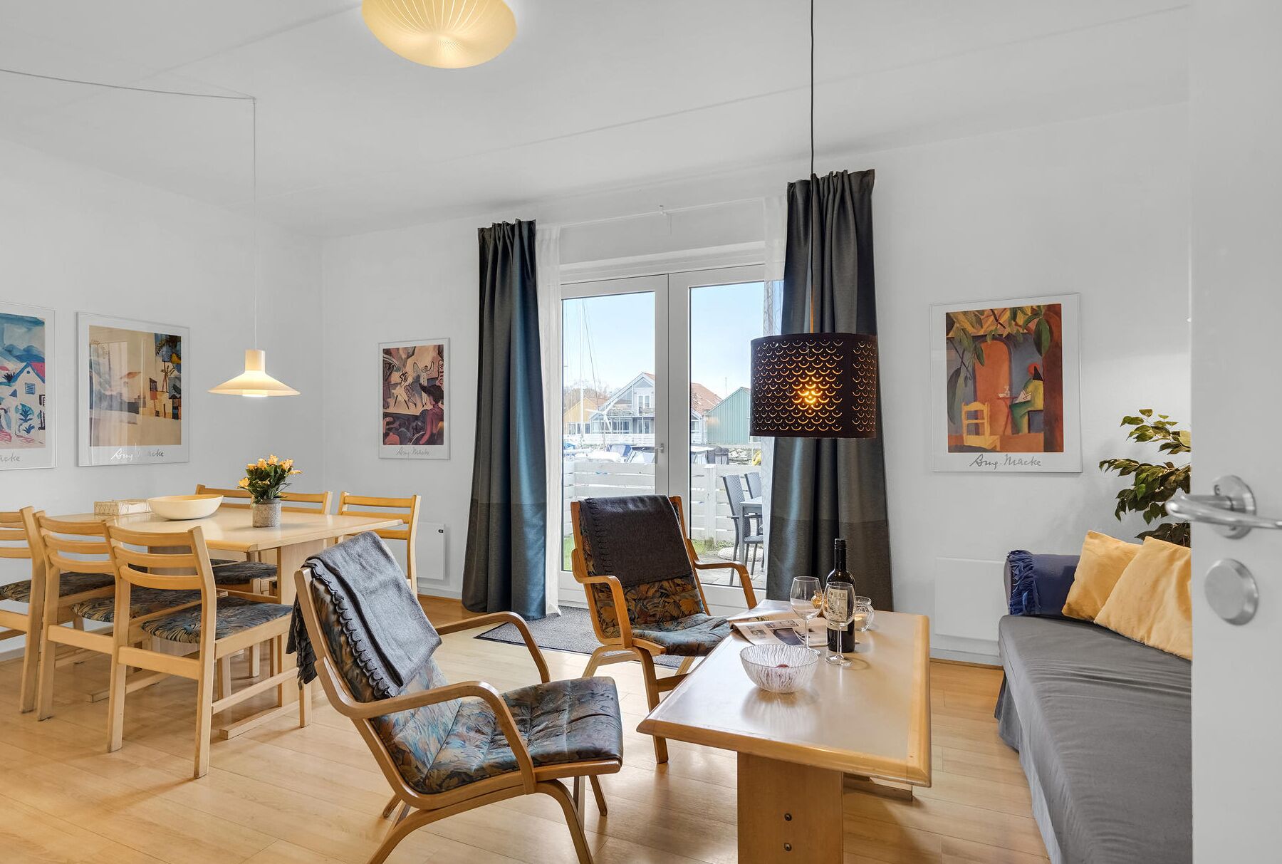 A modern living room with a dining area, featuring wooden furniture, a table with a bowl, and artwork on the walls.