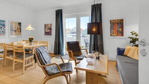 Ein modernes Wohnzimmer mit Essbereich, ausgestattet mit Holzmöbeln, einem Tisch mit Schüssel und Bildern an den Wänden.