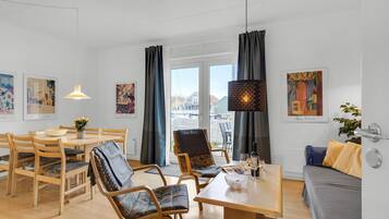 A modern living room with a dining area, featuring wooden furniture, a table with a bowl, and artwork on the walls.