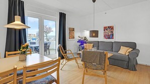 Ein modernes Wohnzimmer mit einem grauen Sofa, Holzstühlen, einem Esstisch und Bildern an den Wänden.