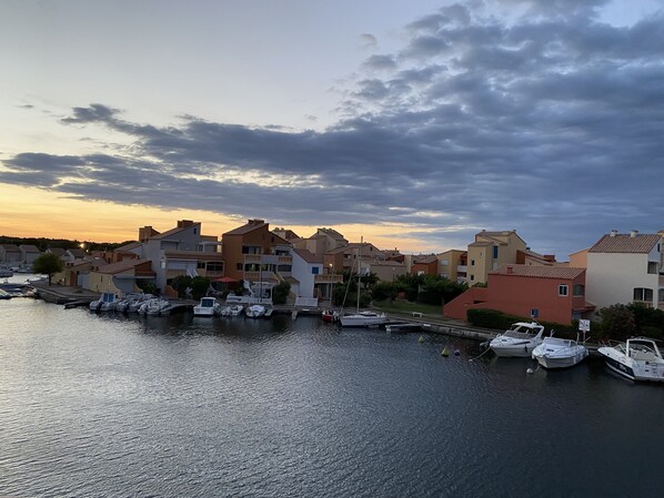 A marina with boats docked, surrounded by residential buildings with balconies and a sunset sky. - A little corner of paradise overlooking the marine lake Le Barcares (Le Barcarès)