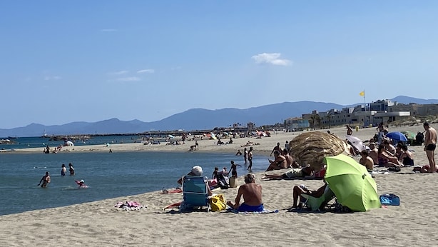 A beach with people sunbathing and swimming. There are umbrellas and beach chairs.