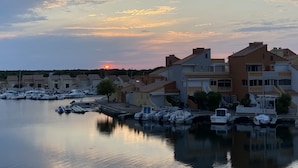 A marina with boats docked, a sunset in the background, and residential buildings with balconies.