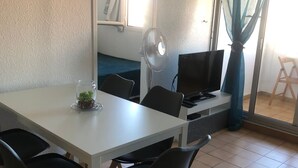 A dining area with a white table, black chairs, a small plant, a fan, and a TV.