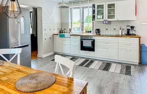 A modern kitchen with white cabinetry, a built-in oven, and a dining area with a wooden table and woven placemat. - 2 bedroom cozy home in Rydsgård (Rydsgård)
