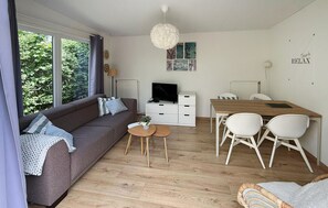 Ein modernes Wohnzimmer mit Sofa, Couchtisch, Fernseher und Essbereich mit Stühlen und Tisch.