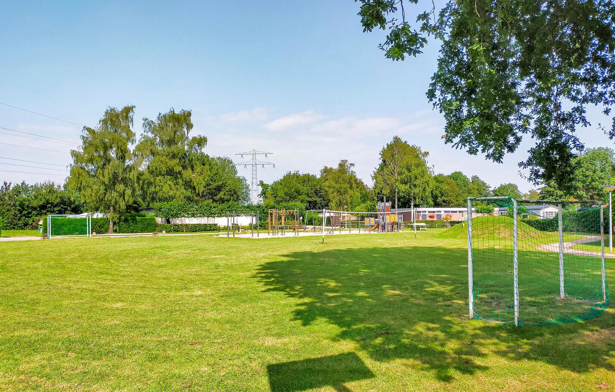 A well-maintained grassy field with a soccer goal, surrounded by trees and a playground.